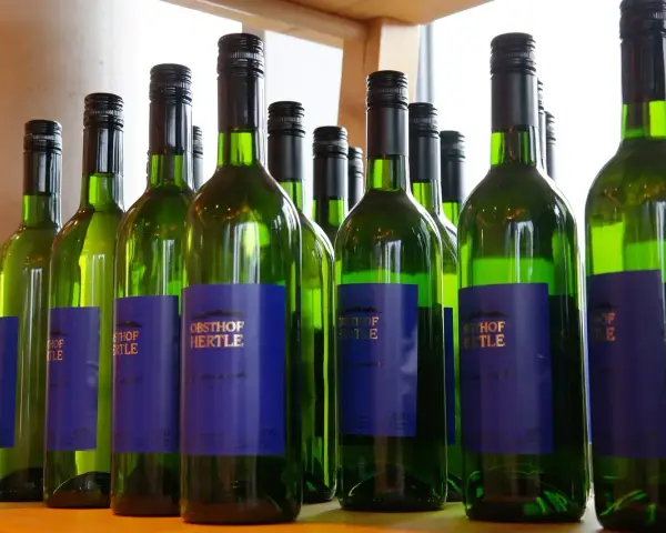 Rząd zielonych butelek białego wina Obsthof Hertle. Lepiej pić drinki czy białe wino? Wybór należy do Ciebie!