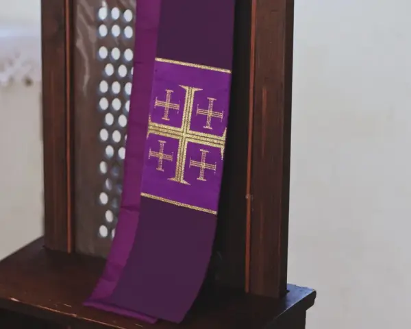 Fioletowa stuła z krzyżami, symbol przygotowania do spowiedzi wielkanocnej, wisi na drewnianej kratce konfesjonału.