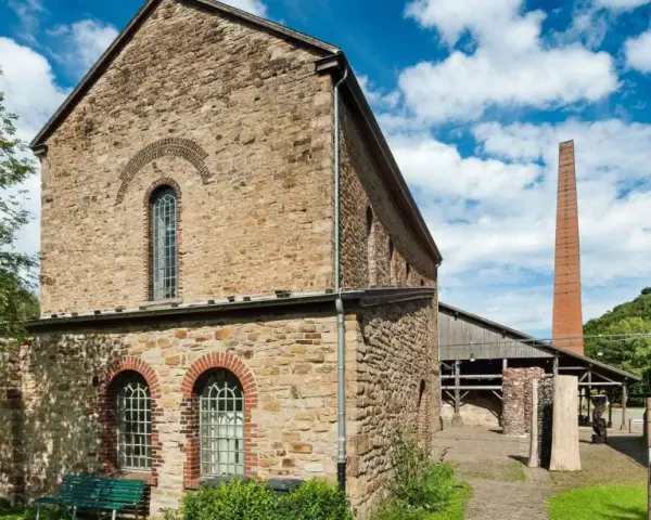 Altes rheinisches Bergwerk mit Backsteinkamin und einem Baum mit roten Beeren.
