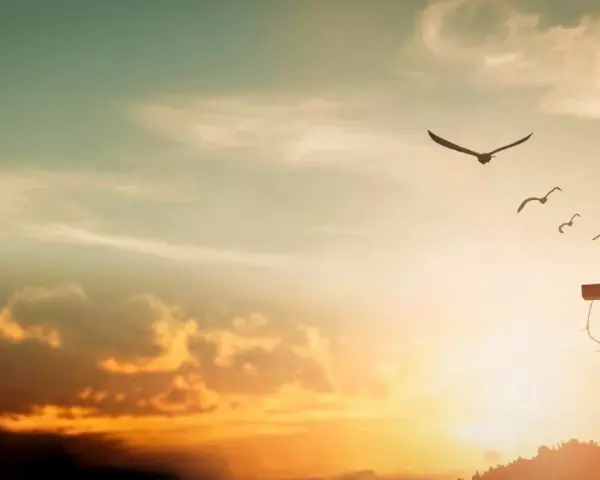 A cross on a hill, adorned with thorns, stands against a sunset sky. Birds fly overhead, symbolizing the feast of the exaltation of the holy cross.