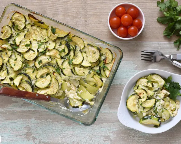 Delicioso calabacín al horno, gratinado y espolvoreado con perejil fresco. Servido en una fuente de vidrio y un plato blanco.