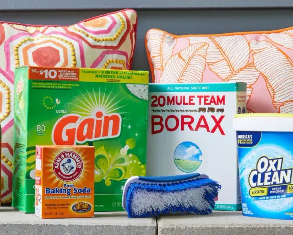 Supplies for how to clean outdoor cushions: Scotchgard, Gain detergent, Borax, baking soda, OxiClean, and a scrub brush.