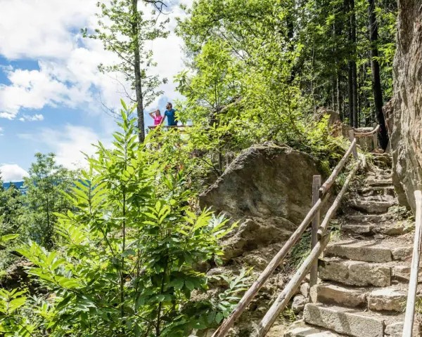 Ein Paar genießt die Aussicht vom Schenner Waalweg. Steintreppen führen durch üppige Vegetation und Felsen.