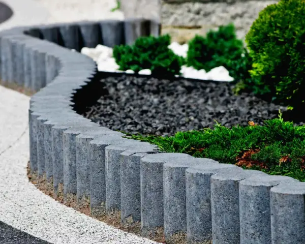 Eleganckie obrzeża trawnikowe z kostki betonowej tworzą falistą linię, oddzielając zadbane rabaty z iglakami od ścieżki.
