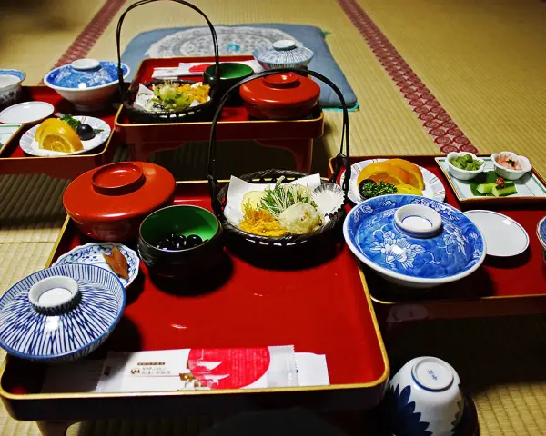 A traditional Japanese meal, perhaps a monk diet, featuring small dishes of tempura, fruit, pickles, and black beans on red lacquer trays.