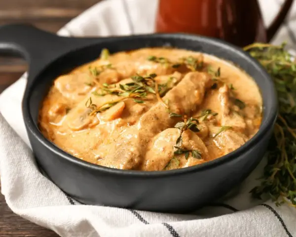 Cremiges Rindfleisch mit Pilzen, garniert mit frischem Thymian. Ein köstliches stroganoff rezept original, serviert in einer schwarzen Schüssel.
