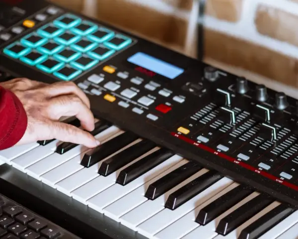 Hand spielt auf einem Keyboard, das für die Erzeugung von Synth-Musik verwendet wird. Viele Knöpfe und Pads sind sichtbar.