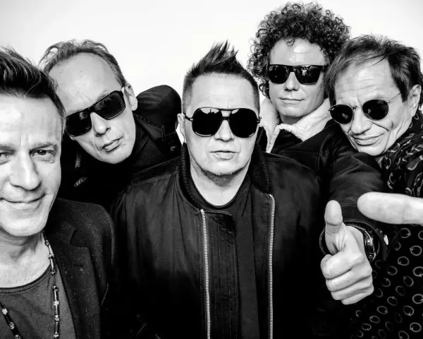 Pięciu mężczyzn w okularach przeciwsłonecznych, gotowych na koncert. Jeden z nich pokazuje kciuk w górę, jakby mówił "t.love hau! hau!".