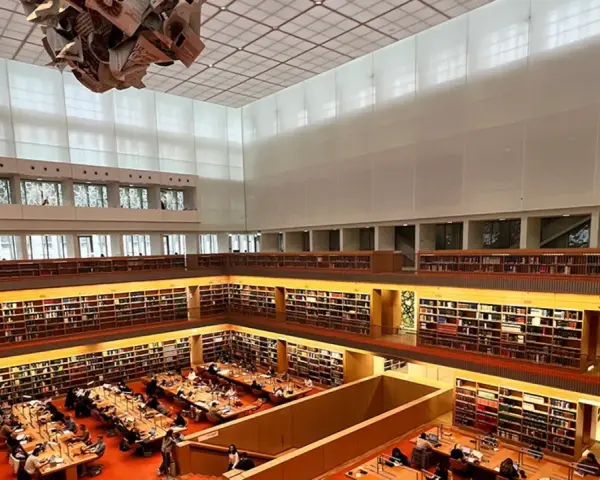 Große Bibliothek mit vielen Regalen voller Bücher. Menschen sitzen an Tischen und lesen. Ein Ort für Lesungen in Berlin.