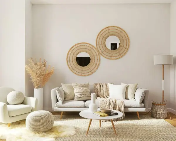 Salón acogedor con butaca blanca y sofá gris, decorado con espejos de mimbre y plantas secas. La combinación de sofá y butaca crea un espacio perfecto para relajarse.