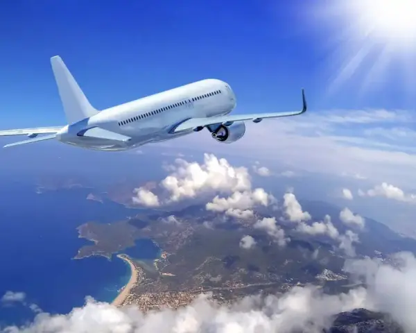 Un aereo bianco solca il cielo azzurro sopra una costa frastagliata. Il sole splende, creando un senso di distacco del vitreo e aereo.