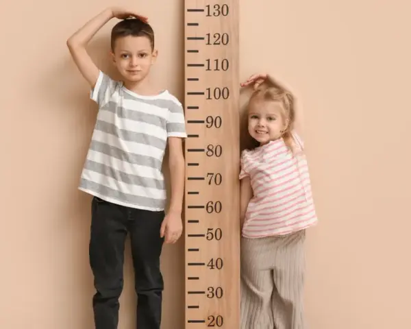 Chłopiec i dziewczynka mierzą wzrost. Chłopiec ma ok. 120 cm, dziewczynka ok. 90 cm. Rozmiar 68 jaki wiek?