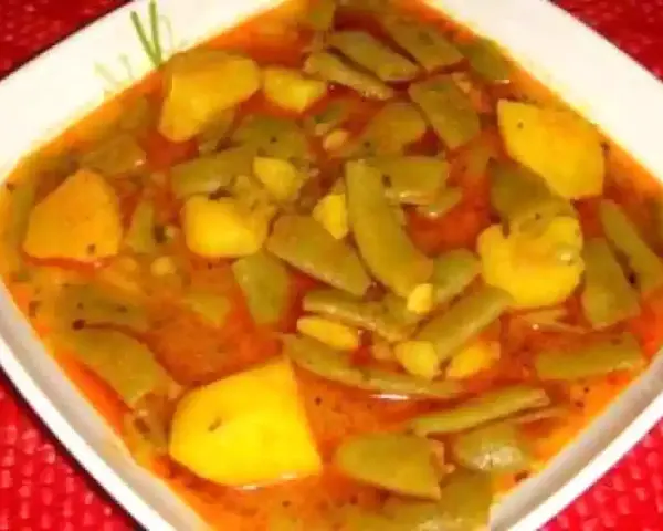 Un plato humeante de judías verdes con patatas, cocinado en una sabrosa salsa rojiza.