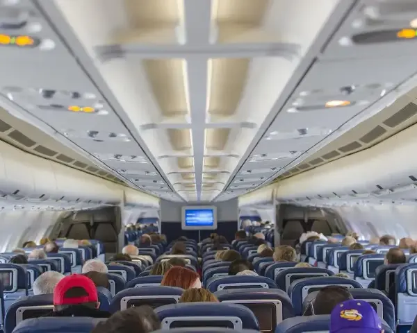 Wnętrze samolotu Boeing 737 Ryanair. Pasażerowie siedzą w rzędach niebieskich foteli, patrząc w stronę kokpitu.