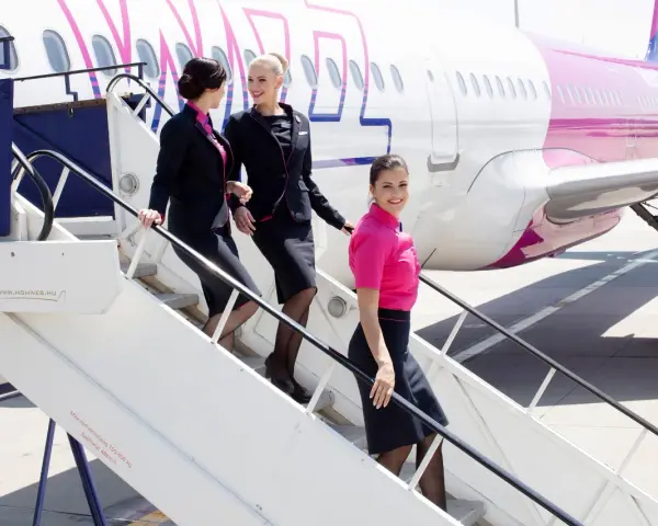 Uśmiechnięte stewardessy Wizz Air schodzą po schodkach. Ciekawe, ile zarabia stewardessa Wizz Air za taką pracę?