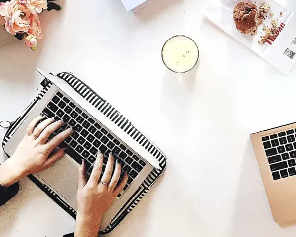 Kobieta pisze na laptopie, przygotowując wypowiedzenie umowy o dzieło. Obok świeca, muffinka i bukiet kwiatów.