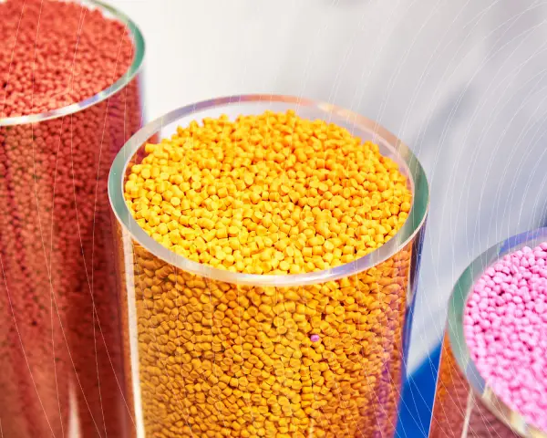 Trzy przezroczyste cylindry wypełnione kolorowymi granulkami plastiku: czerwonym, żółtym i różowym.