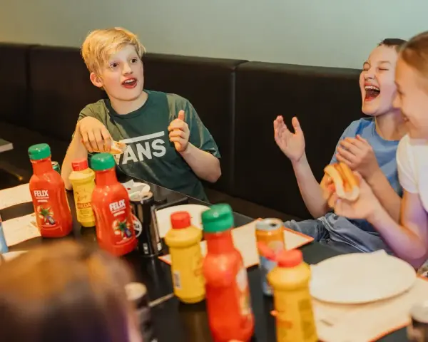 Barn skrattar och äter korv med bröd vid ett bord med Felix ketchup och senap. Perfekt för tips på femkamp!
