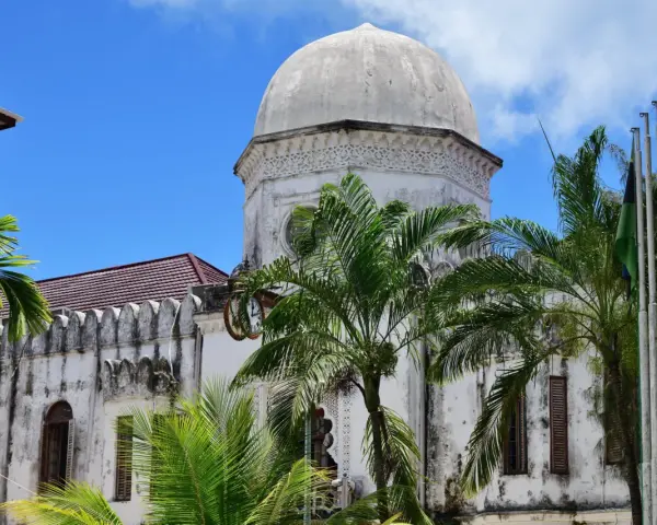 Biała, zabytkowa budowla z kopułą i palmami na tle błękitnego nieba. Klimatyczne zanzibar miasto.