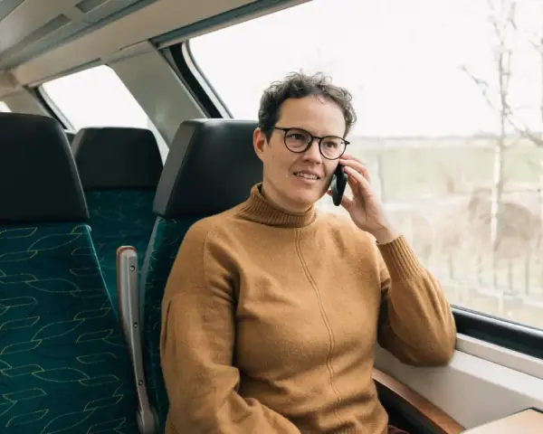 Kobieta w brązowym swetrze rozmawia przez telefon w pociągu. Czas na moją kolej, by usiąść przy oknie i podziwiać widoki.