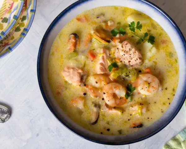 Sopa cremosa de pescado con salmón, gambas y mejillones, decorada con perejil.