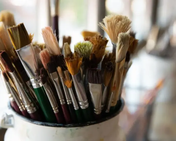 Gros plan sur un pot rempli de pinceaux de peinture aux poils variés, certains neufs, d'autres usagés.