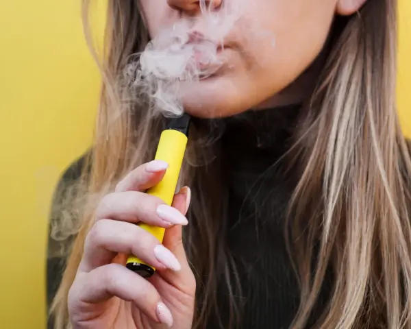 Mujer exhala vapor de un vaper sin nicotina, pero ¿sabías que el vaper sin nicotina mancha los dientes?