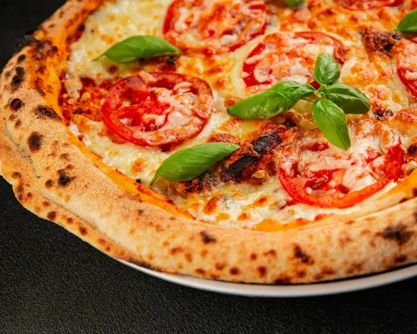 Pyszna pizza Margherita z pomidorami i bazylią, idealnie wypieczona w wysokiej temperaturze przez kilka minut.