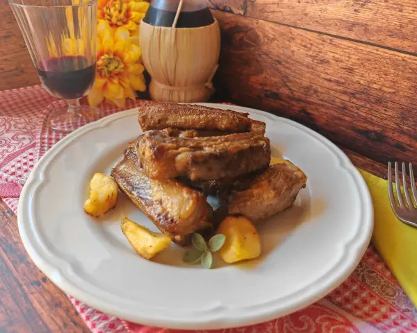 Succulente costine di maiale in padella, dorate e saporite, servite con patate arrosto e un rametto di salvia.