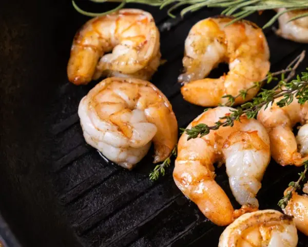 Gambas a la plancha jugosas y doradas, con ramitas de tomillo fresco sobre una sartén de hierro fundido.