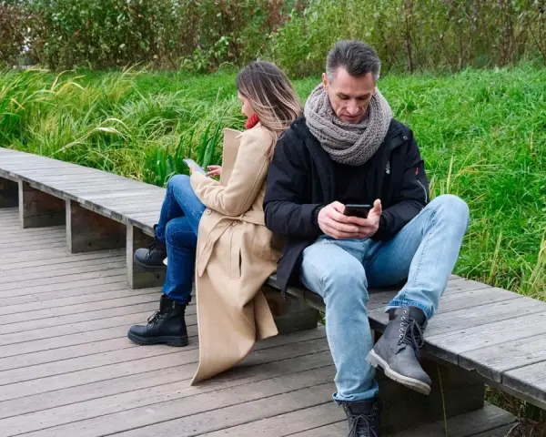 Para, siedząc tyłem do siebie na ławce, wpatruje się w telefony. Może szukają inspiracji, co napisać do dziewczyny, zamiast rozmawiać?