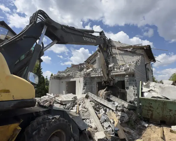 Koparka Volvo niszczy budynek. Trwa rozbiórka budynku, cena za m2 jest kluczowa przy planowaniu prac.
