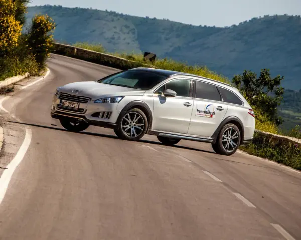 Białe kombi Peugeot 508 RXH na krętej drodze w górach.