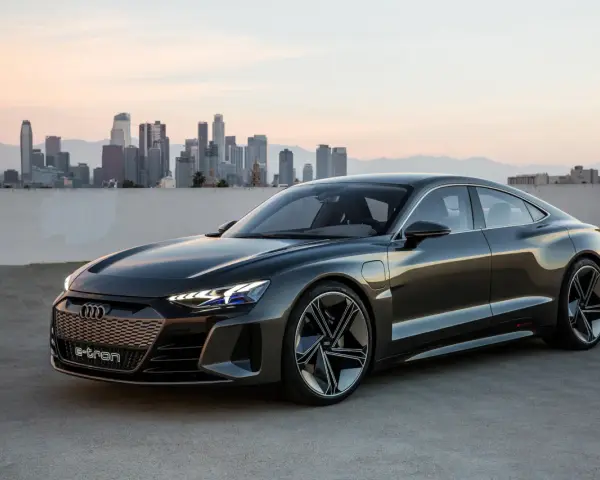 Ciemnoszary Audi e-tron GT stoi na tle panoramy miasta o zachodzie słońca.