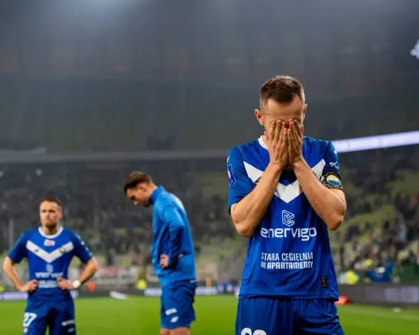 Piłkarz w niebieskiej koszulce z napisem "enerVigo" zakrywa twarz dłońmi. W tle inni zawodnicy i trybuny. Emocje po przegranym meczu w I lidze piłki ręcznej.