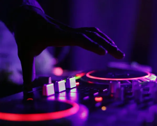 Dłoń DJ-a nad konsolą, czerwone i fioletowe światła. To właśnie tak tworzy się dubstep, co to za muzyka?