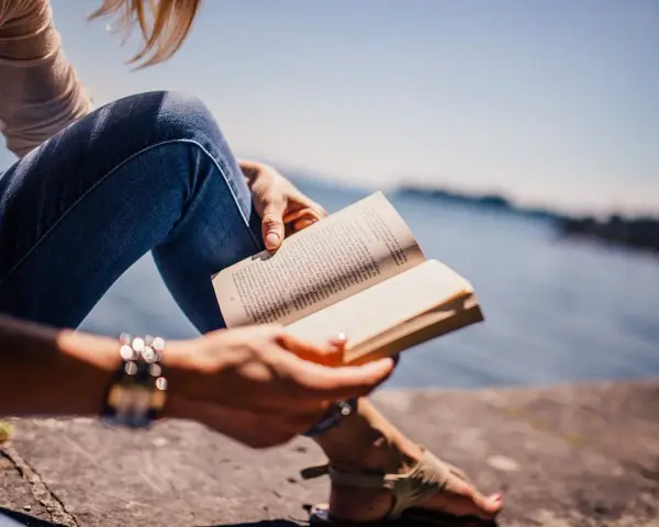 Persona sentada junto al agua, leyendo un libro en francés.