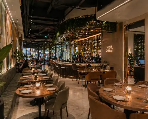Elegantes mesas y un bar iluminado, con arte mural y plantas, ofrecen **ideas decoración restaurante** acogedoras.
