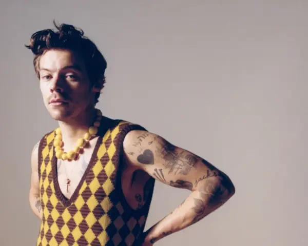 Harry Styles w kamizelce w romby i żółtym naszyjniku, jakby inspirował nowe harry styles utwory.