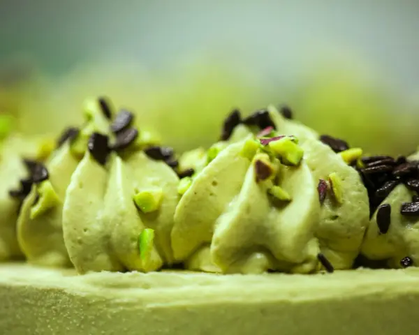 Delikatna masa pistacjowa ozdobiona kawałkami pistacji i czekolady, tworząca apetyczny deser.