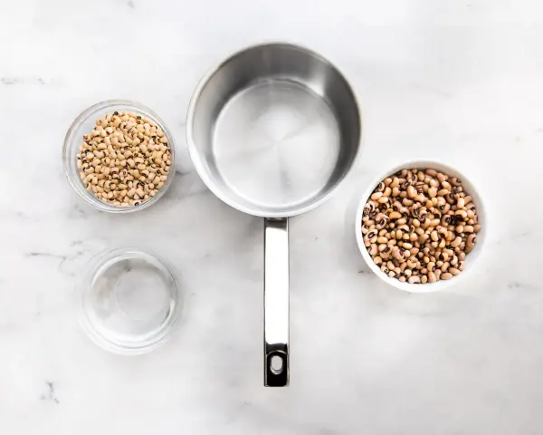 Vorbereitung zum Bohne kochen: zwei Schüsseln mit Schwarzaugenbohnen, ein Topf und eine Schüssel Wasser auf Marmoruntergrund.