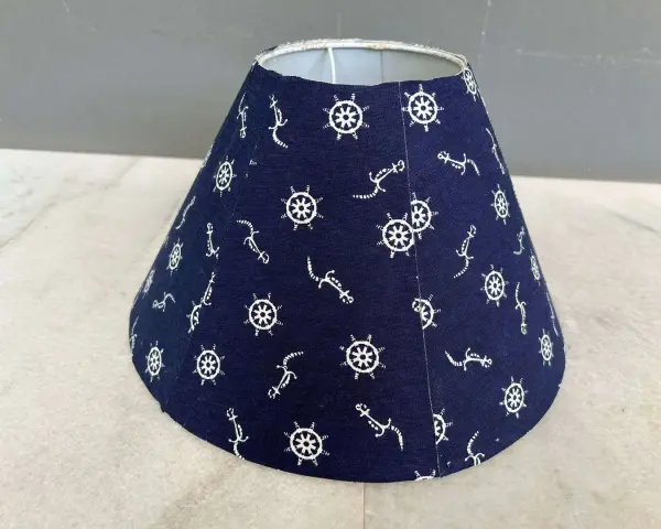 Un abat-jour conique bleu marine orné de motifs d'ancre et de roue de gouvernail. Idéal pour fabriquer un abat-jour en tissu plissé avec une touche marine.
