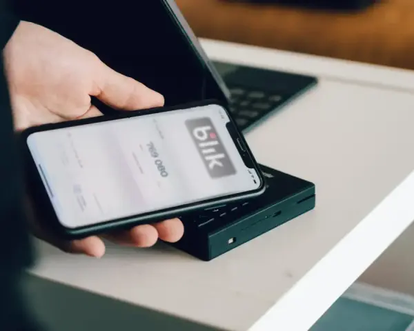 Dłoń trzyma smartfon z aplikacją Blik i kodem transakcji nad terminalem płatniczym.