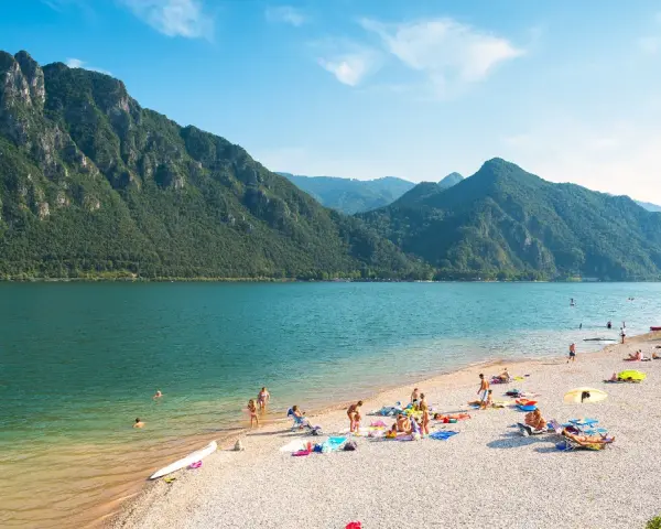 Spiaggia affollata sui laghi in Piemonte, ideale per una gita in moto. Montagne verdi e acqua azzurra.