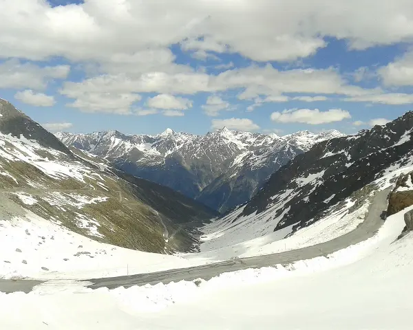 Strada tortuosa sulla Ötztaler Gletscherstraße, tra montagne innevate e cielo azzurro con nuvole bianche.