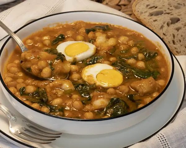 Potaje de garbanzos con bacalao y huevo duro en un cuenco blanco.
