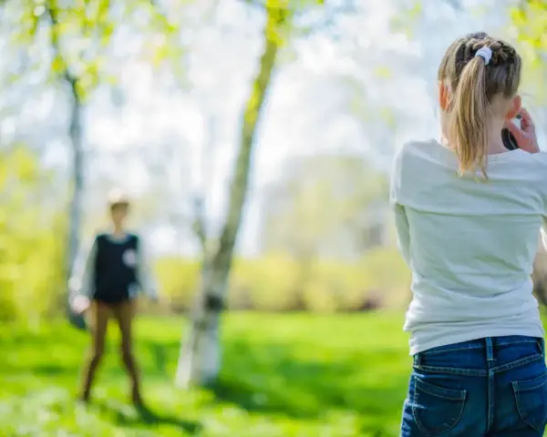 Flicka med flätat hår tar bild på en annan person under en tipspromenad. Soligt och grönt i parken.