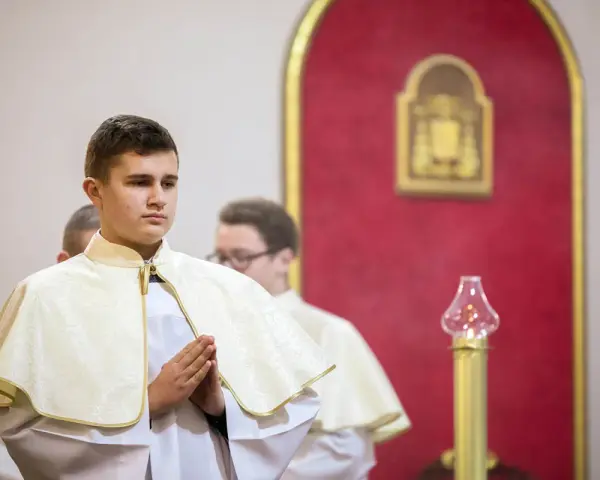 Junge Männer in festlicher Kleidung, die auf ihre Diakon Ausbildung vorbereitet werden. Sie stehen betend in einer Kirche.