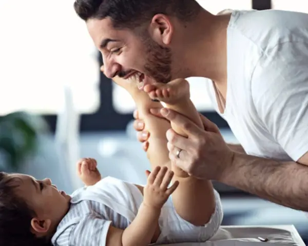 Ein lachender Vater mit Kind spielt liebevoll mit den Füßen seines Babys.