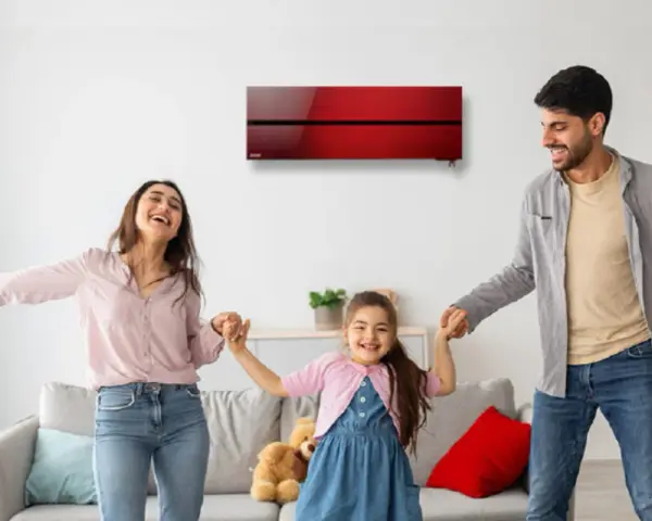 Familia feliz bailando en una sala con aire acondicionado inverter rojo. Disfrutan del confort y bajo consumo kwh.